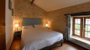 A bedroom with a stone wall, a wooden bed frame, two bedside lamps, and a window with curtains. - Two Bedroom House in Domaine les Granges (Ternant)