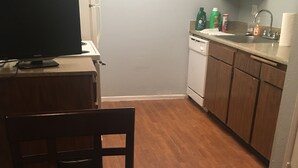 A compact kitchen with wooden cabinets, a white refrigerator, a dishwasher, and a small table with a candle.
