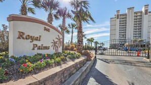 Un panneau indiquant « Royal Palms », avec le numéro « 561 », et une entrée fermée par un portail, donnant sur un espace de stationnement.