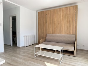 Un salon moderne avec une armoire en bois, un canapé beige et une table basse blanche.