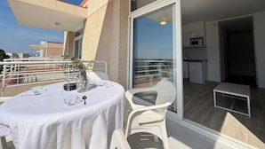 Un balcon avec une table dressée pour deux personnes, une chaise et un pot de fleurs.