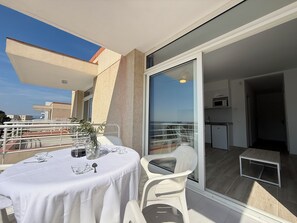 A balcony with a table set for two, a chair, and a potted plant.