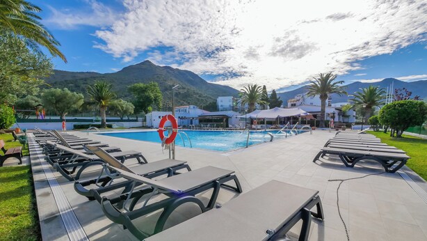 A poolside area with lounge chairs and a lifebuoy, surrounded by greenery and mountains.