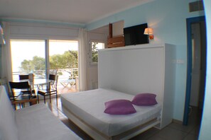 A room with a bed, a TV mounted on the wall, a chair, and a table.