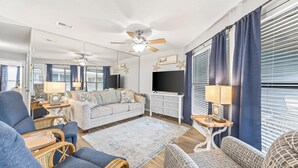 Una sala de estar con sofá, sillones, televisor y ventilador de techo.