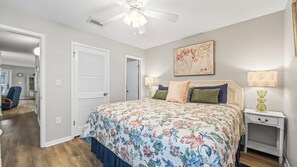 Een slaapkamer met een bloemenbedekker, een plafondventilator, een bedlamp en een ingelijst kunstwerk aan de muur.