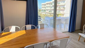 A room with a wooden dining table, white chairs, a TV mounted on the wall, and a view of a balcony with outdoor seating. - Agi Rescator 302 Apartamento for rent in Roses Girona. (Roses)