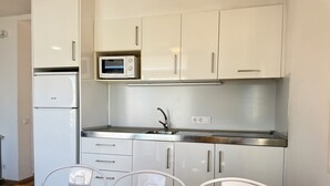 A compact kitchen with white cabinets, a microwave, a refrigerator, and a sink. There are two chairs at a wooden table. - Agi Rescator 302 Apartamento for rent in Roses Girona. (Roses)