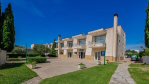 A multi-story residential building with a paved courtyard, potted plants, and a clear blue sky. - Agi Rescator 122 Apartamento for rent in Roses Girona. (Rosas / Roses)