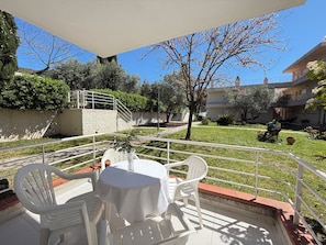 An outdoor patio with a table and chairs, surrounded by a white railing, with a clear view of the courtyard and buildings in the background. - Agi Rescator 122 Apartamento for rent in Roses Girona. (Rosas / Roses)