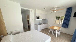 A bedroom with a bed, a wooden table, and a kitchen area with a microwave. - Agi Rescator 122 Apartamento for rent in Roses Girona. (Rosas / Roses)