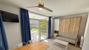 A modern room with a wooden table, white chairs, a sofa, a ceiling fan, and a TV mounted on the wall. - Agi Rescator 122 Apartamento for rent in Roses Girona. (Rosas / Roses)