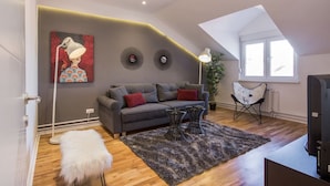 A modern loft apartment with a sloped ceiling, a grey sofa with red cushions, a black coffee table, a white furry ottoman, and a large painting on the wall. - Amazing design, Huge, Prime location, With Parking (Stari Grad)