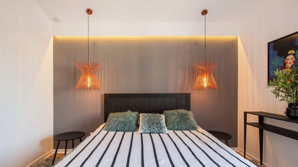 A modern bedroom with a large bed, two wall-mounted lamps, a dark headboard, and a small side table. - Amazing design, Huge, Prime location, With Parking (Stari Grad)
