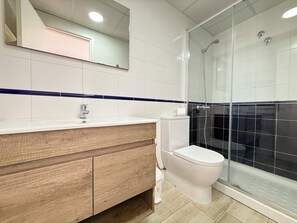 Une salle de bain moderne avec un meuble-lavabo en bois, un lavabo blanc et une cabine de douche en verre.