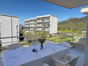 A balcony with a table set for dining, overlooking a building and a mountainous landscape. - Agi Rescator 104 Apartamento for rent in Roses Girona. (Rosas / Roses)