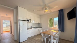 A modern kitchen with white cabinets, a microwave, and a dining area with a wooden table and white chairs. - Agi Rescator 104 Apartamento for rent in Roses Girona. (Rosas / Roses)