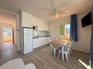 A modern kitchen with white cabinets, a microwave, and a dining area with a wooden table and white chairs. - Agi Rescator 104 Apartamento for rent in Roses Girona. (Rosas / Roses)