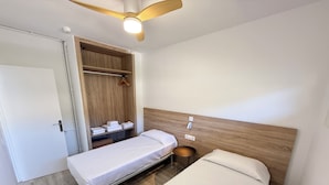 Ein kleines Hotelzimmer mit zwei Betten, einem Holzschrank, einem Deckenventilator und einem Nachttisch.