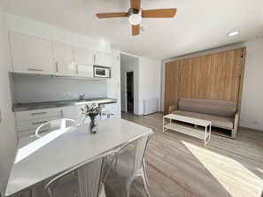 A modern kitchen with white cabinets, a dining table with chairs, a ceiling fan, and a wooden panel wall. - Agi Rescator 105 Apartamento for rent in Roses Girona. (Rosas / Roses)