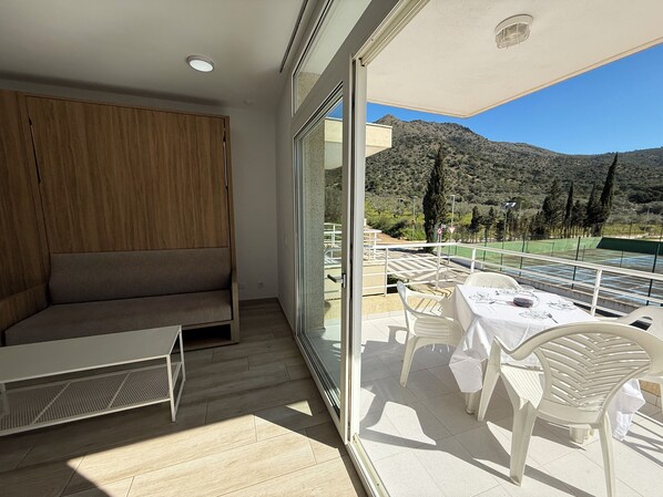 A balcony with a view of a mountain, a table with chairs, and a sofa.