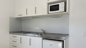 Ett kök med vita skåp, en mikrovågsugn, en diskho i rostfritt stål och en diskmaskin.
