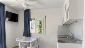 Een compacte, moderne keuken met een eettafel en stoelen, een plafondventilator, een flatscreen-tv en een raam met gordijnen.