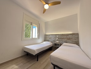 A room with two single beds, a ceiling fan, a window with a view of greenery, and a wall-mounted nightstand. - Agi Rescator 329 Apartamento for rent in Roses Girona. (Rosas / Roses)