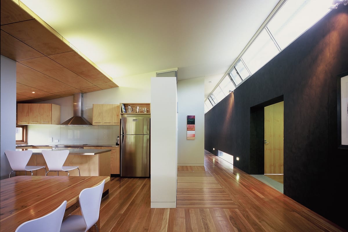 A modern kitchen with wooden cabinets, a stainless steel refrigerator, and a dining area with a wooden table and white chairs.