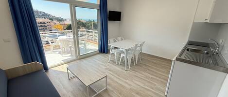 Ein modernes Zimmer mit Balkon, Esstisch mit Stühlen, einer Küchenzeile und einem Deckenventilator.