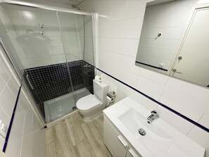 Un baño con ducha, inodoro, lavabo y espejo.