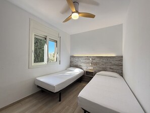 A bedroom with a bed, a bench, a ceiling fan, a window, and a wall-mounted light fixture.
