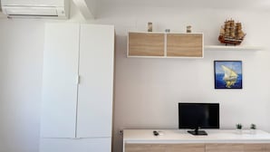 A modern living room with a white wardrobe, a flat-screen TV, a small cabinet with decorative items, and a ship model on a shelf.