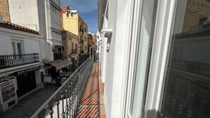 A narrow street with buildings on either side, a balcony with a metal railing, and a restaurant sign. - Agi Joan Badosa 1A Apartamento for rent in Roses Girona. (Rosas / Roses)