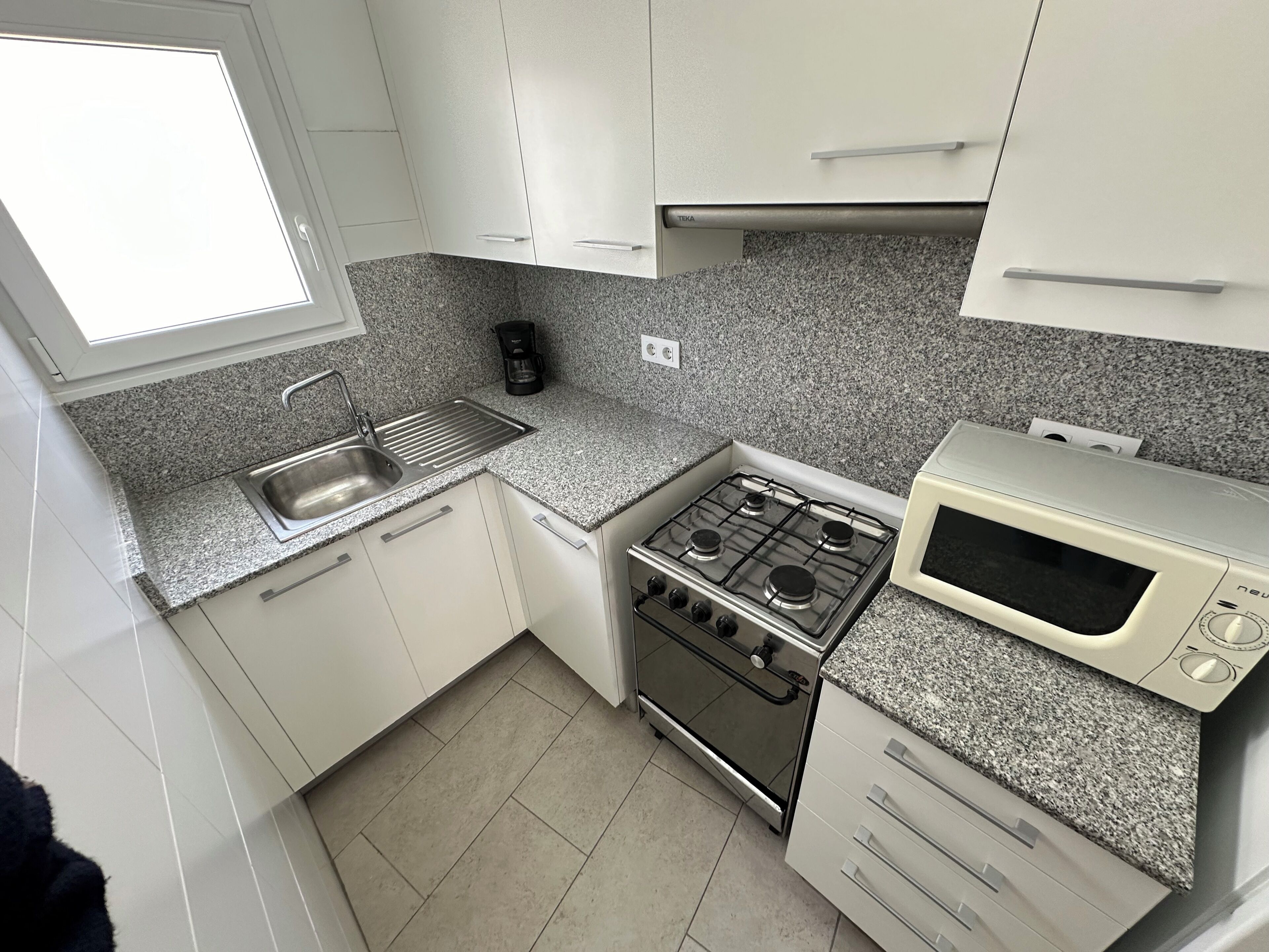 Una cucina compatta con mobili bianchi, un piano di lavoro in granito, un fornello a gas, un forno a microonde e una macchina da caffè.