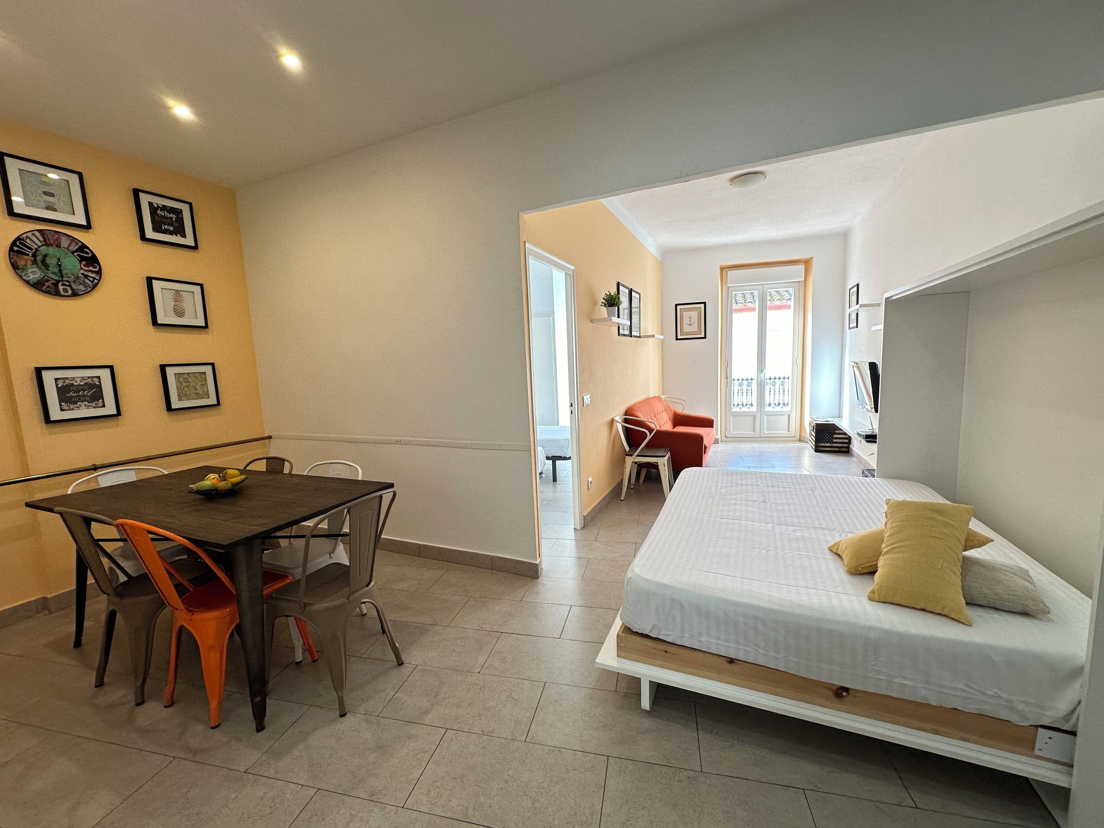 Une pièce de taille modeste comprenant un lit, une table à manger avec des chaises et un petit coin salon avec un fauteuil.