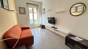 A living room with a sofa, a television, a wall-mounted shelf, and a door leading outside. - Agi Joan Badosa 1A Apartamento for rent in Roses Girona. (Rosas / Roses)