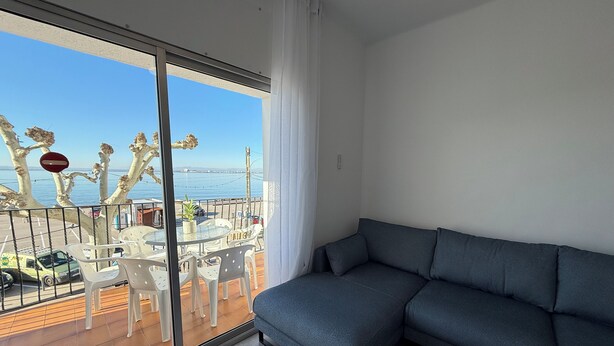 En balkong med utsikt över havet, en soffa och ett matbord med stolar.