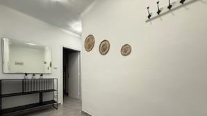 En hall med en vit vägg, en spegel, tre dekorativa tallrikar och ett svart metallställ med krokar.