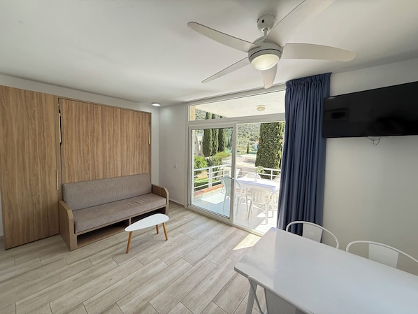 A modern room with a wooden wardrobe, a grey sofa, a small table, and a ceiling fan.