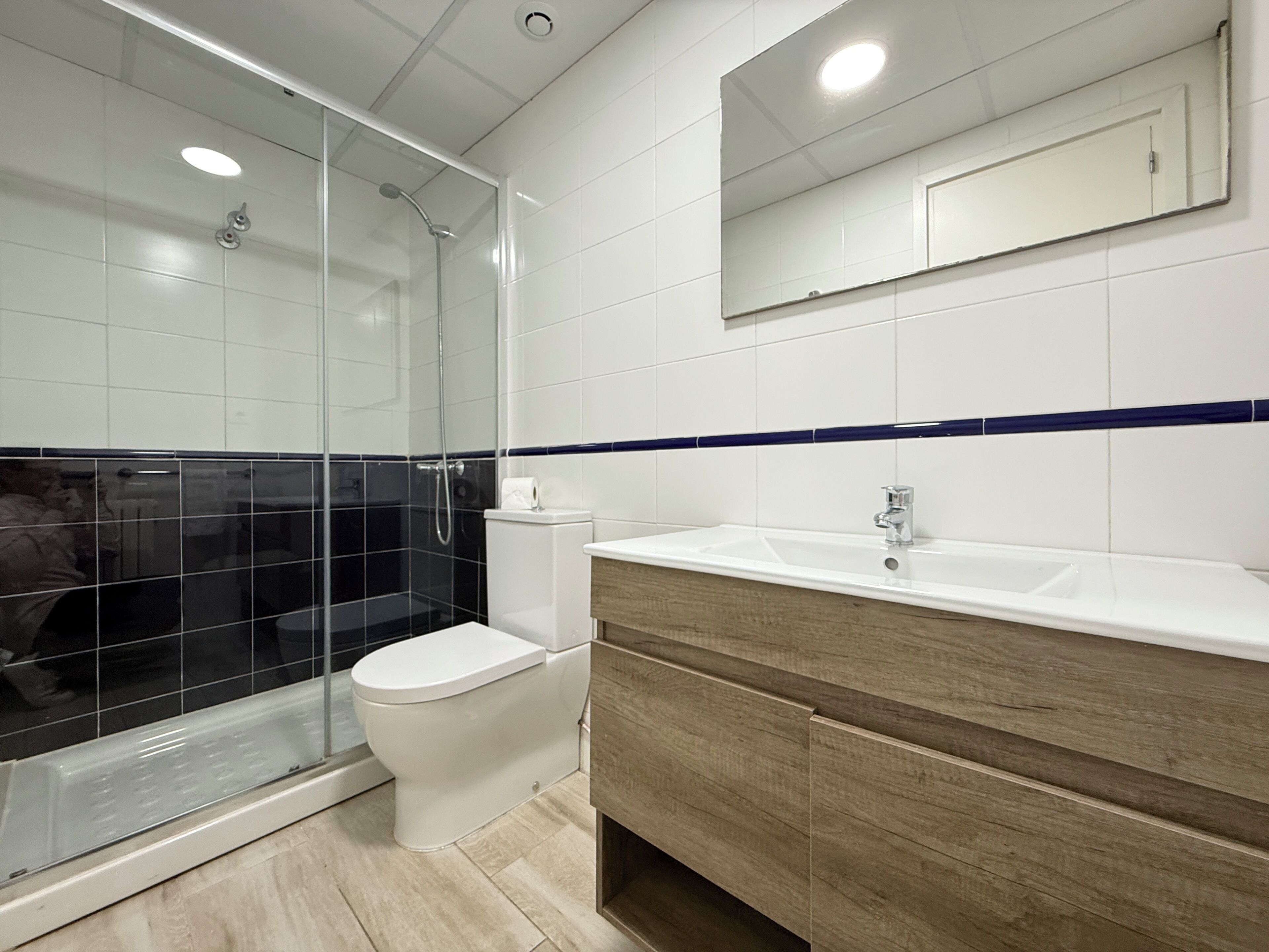 Ein modernes Badezimmer mit einer Duschkabine aus Glas, einer weißen Toilette, einem hölzernen Waschtisch und einem Spiegel über dem Waschbecken.