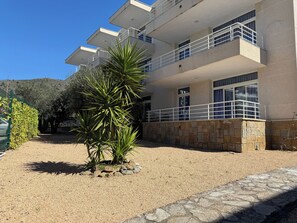 A multi-story building with balconies, a gravel driveway, and a stone wall.