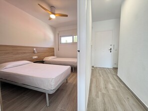 Une chambre d’hôtel avec deux lits, un ventilateur de plafond, une fenêtre et une porte.
