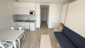 Een kleine keuken met een magnetron, gootsteen en vaatwasser, een eethoek met stoelen, en een bank in een woongedeelte.