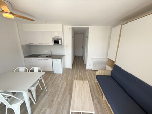 Une cuisine compacte équipée d’un four à micro-ondes, d’un évier et d’un lave-vaisselle, un coin repas avec des chaises et un canapé dans l’espace de vie.