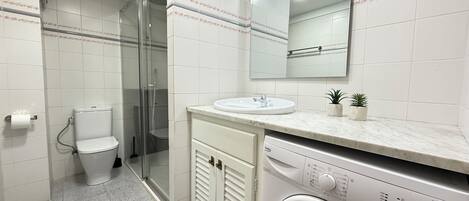 A modern bathroom with a glass-enclosed shower, a toilet, a sink, and a front-loading washing machine.