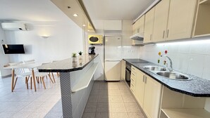 Une cuisine moderne dotée d’un îlot central, de meubles blancs, d’un four à micro-ondes encastré et d’un évier en acier inoxydable.