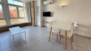 Une pièce moderne équipée d’une table et de chaises, d’un téléviseur fixé au mur et de grandes fenêtres avec des rideaux.