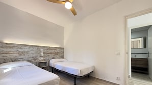 A bedroom with two beds, a ceiling fan, a wooden headboard, and a view into the bathroom. - Agi Rescator 321 Apartamento for rent in Roses Girona. (Rosas / Roses)