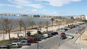 A coastal road with parked cars, a pedestrian walkway, and buildings in the background. - Agi Pi Sunyer 4 1A Apartamento for rent in Roses Girona. (Roses)